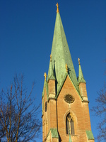 A church steeple roofed in pale green metal pokes up into a clear blue sky.  At lower left some bare trees are lit by the low winter sun.