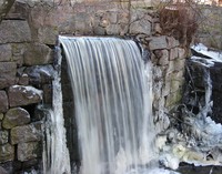A stream flows over a stone wall, icicles hang around it.