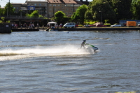 A jetski shoots across the picture from right to left, in the background are the far bank of the river and the railway station.