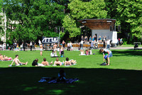 People lying in the sunshine on the grass in front of a stage.  On the stage several girls are dancing.
