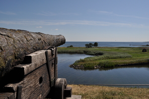 A rusted cannon sits on a wooden carriage, pointing out into the clear blue sky over the sea.